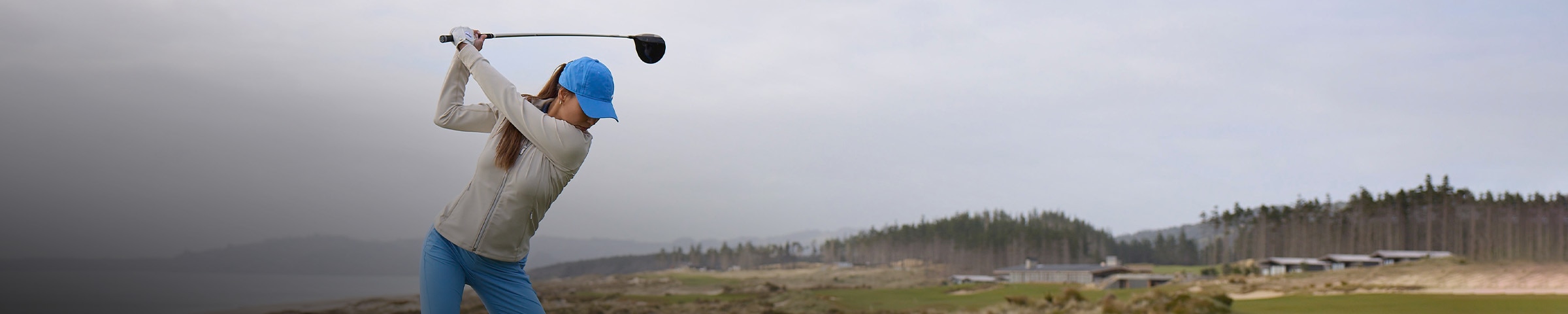 A woman wearing a KJUS Birdie Midlayer Jacket tees off on a golf course.